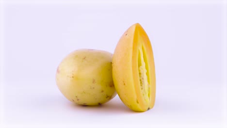 one whole and one half cut mature yellow pepino fruits rotating on the turntable. isolated on the white background. closeup. macro.