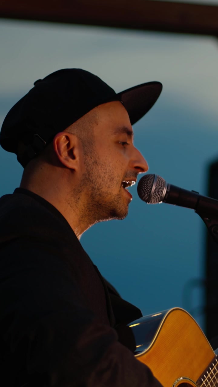 Man Singing and Playing Acoustic Guitar at an Outdoor Evening Performance