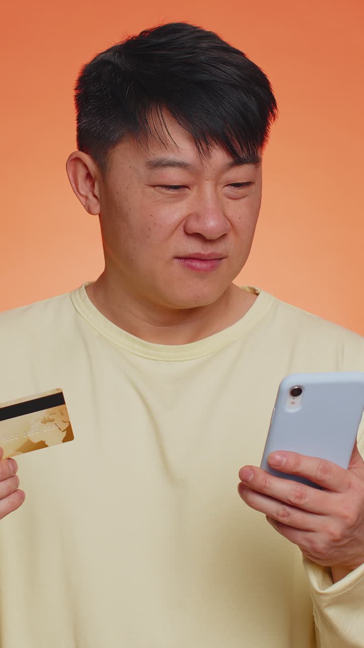 Pria Asia menggunakan kartu bank kredit dan ponsel cerdas saat mentransfer uang pembelian belanja online