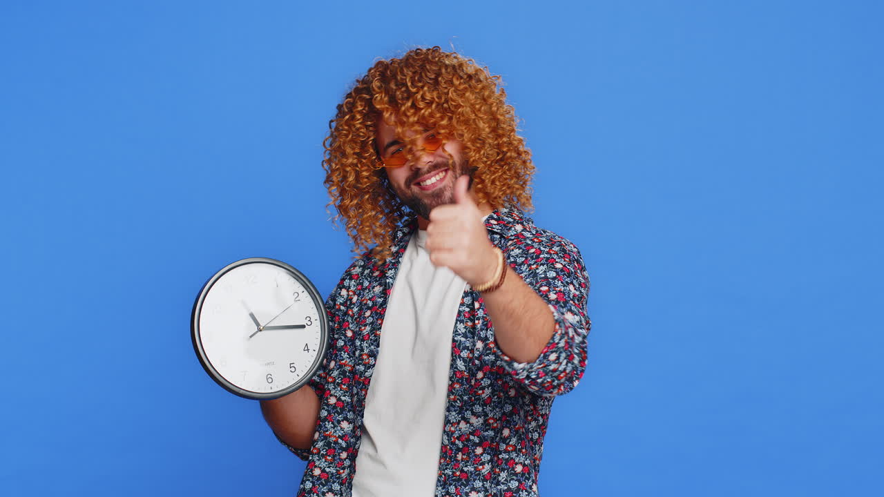 hombre caucásico emocionado mostrando la hora hora en el reloj de la oficina de la pared ok pulgar hacia arriba aprobar apresurarse plazo