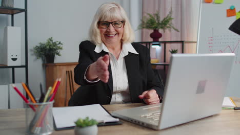 senior business woman employee outstretching hand to camera offering handshake, greeting, welcoming