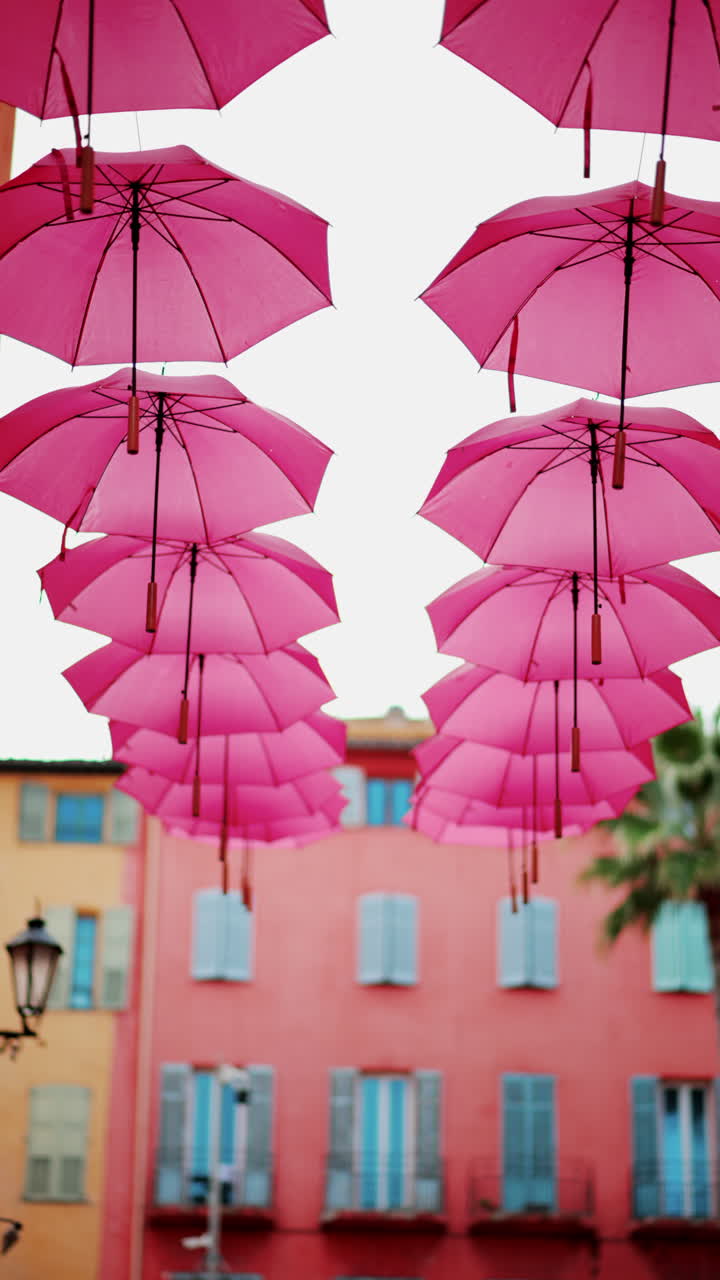 Rows of pink umbrellas above the streets of the old town in Grasse, France. Vertical