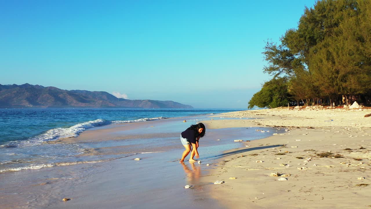 열대 섬의 조용한 모래 해변을 씻는 푸른 바다의 파도와 맨발로 노는 외로운 소녀, 필리핀의 맑고 밝은 하늘