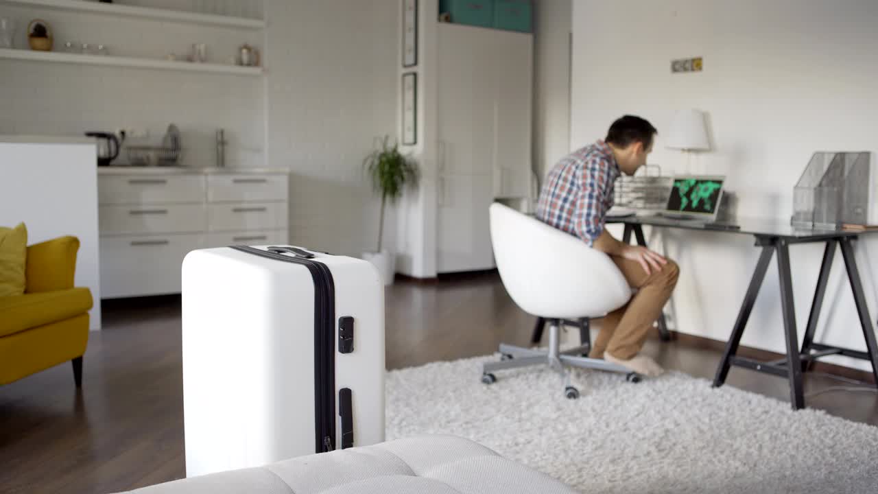 노트북으로 인터넷을 탐색하고 전 세계적인 팬데 발발을 가진 지도를 만난 한 남자가 휴대 전화로 항공편 취소를 가진 sms를 확인하고 짐을 풀고 있습니다.