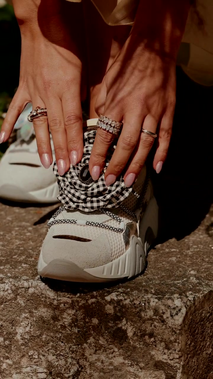 Mani femminili con anelli che sistemano una sneaker bianca decorata con un fiore di tessuto a quadri su pietra