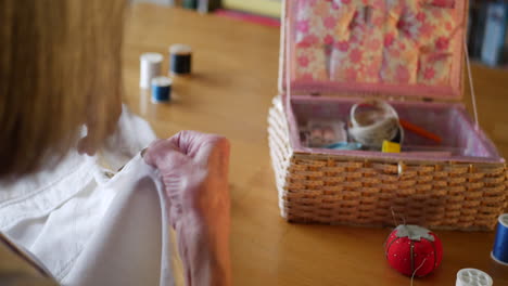 una anciana cosiendo a mano un nuevo botón en una camisa blanca para repararlo con su aguja e hilo