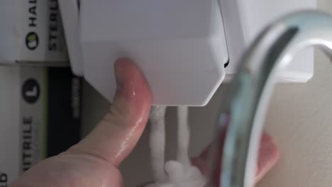 a person is seen squirting soap onto their hand. medical gloves can be seen nearby.