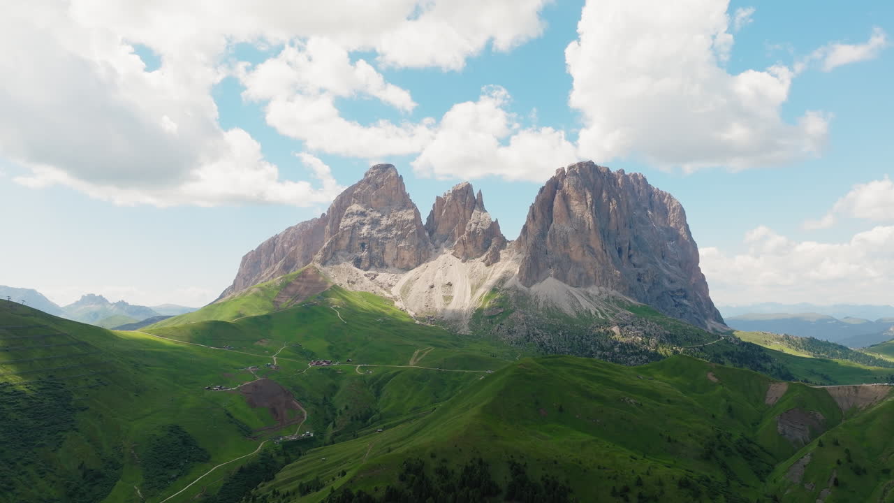 Drone video of the majestic Sassolungo massif captured in spring, where the rugged cliffs meet vibrant grasslands and fresh mountain air fills the scene