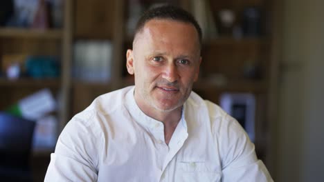 y un hombre adulto con paja en una camisa blanca se sienta en un café sonriendo y posando para la cámara