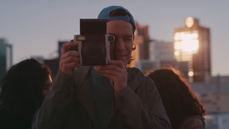 Amigos-Felices-Pasando-El-Rato-En-La-Azotea-Joven-Usando-Una-Cámara-Polaroid-Fotografiando-La-Celebración-De-La-Fiesta-De-Fin-De-Semana-Al-Atardecer