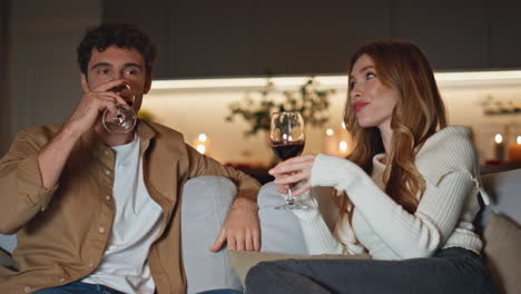 Married pair enjoy date on cozy home couch clinking wine glasses close up.