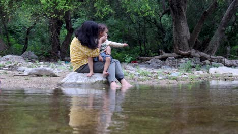 isolated woman spending quality time with son on stone at calm lake shore in the morning