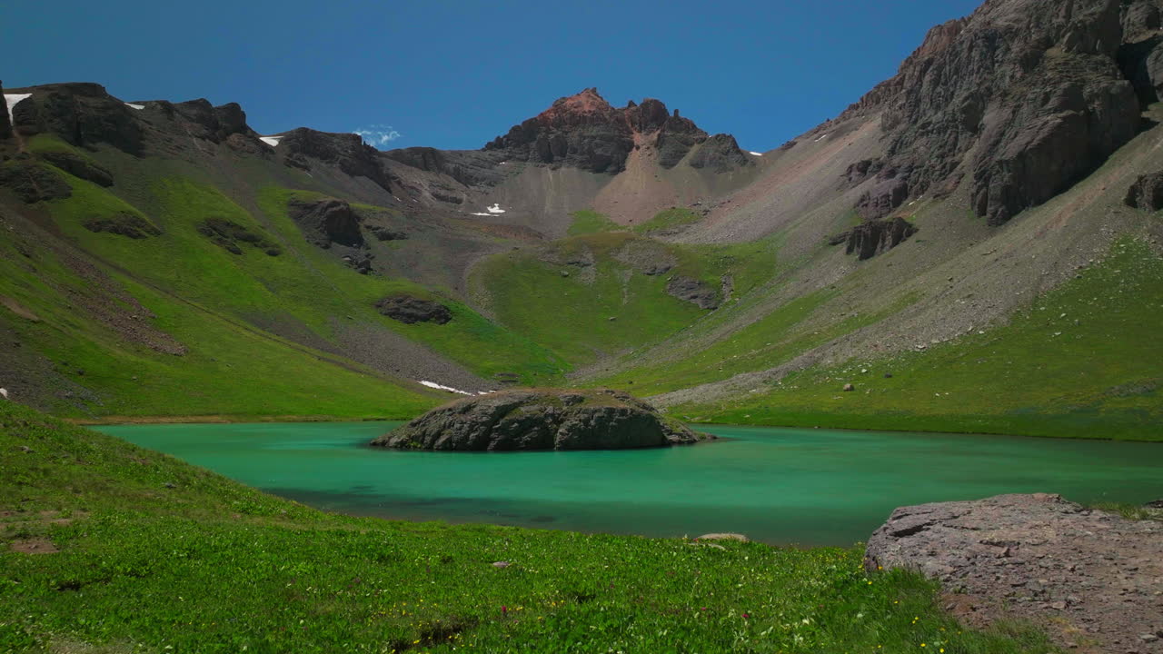 영화 공중 드론 꿈같은 천국 섬 실버턴 호수 얼음 호수 유역 비현실적인 카리브해 아쿠아 블루 실버턴 콜로라도 울창한 녹색 야생 꽃 여름 눈 녹는 바위 산 앞으로의 움직임