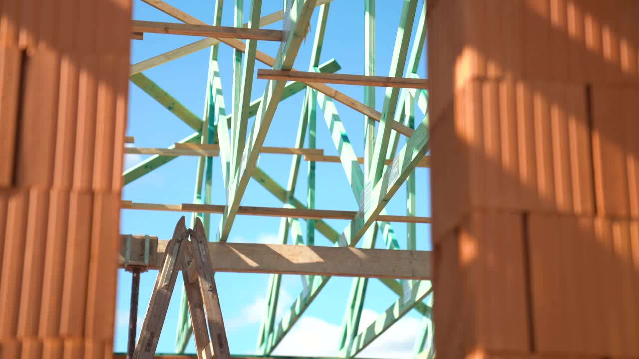 View through brick wall opening showing wooden roof trusses under blue sky
