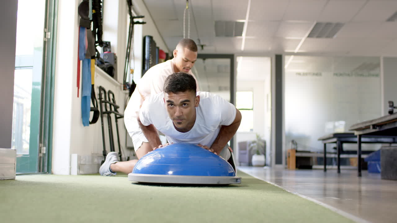 Man in rehabilitation center doing push-ups on balance trainer with therapist