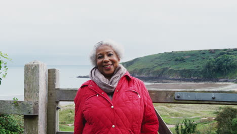 Portrait-Of-Active-Senior-Woman-Walking-Along-Coastal-Path-In-Fall-Or-Winter