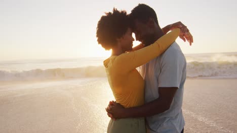 una pareja afroamericana sonriente abrazándose en el agua en una playa soleada
