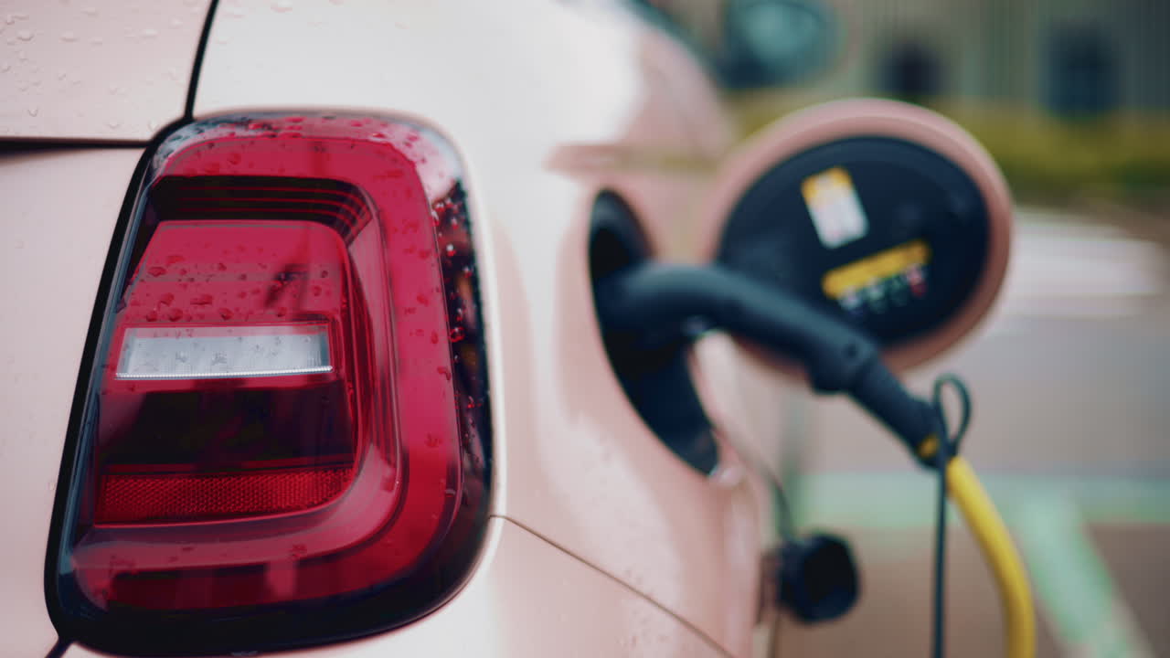 Close up of a pink, electric car charging outdoors under rain