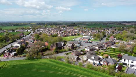 Aerial-rising-view-rural-British-countryside-village-surrounded-by-farmland-fields,-Cheshire,-England