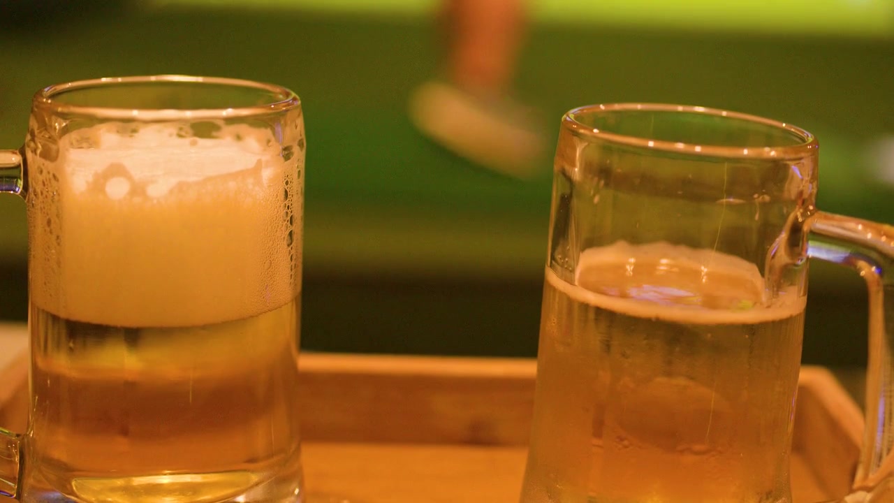 Due boccali di birra lager fredda sono posizionati su un vassoio di legno davanti a uno schermo di simulatore di golf