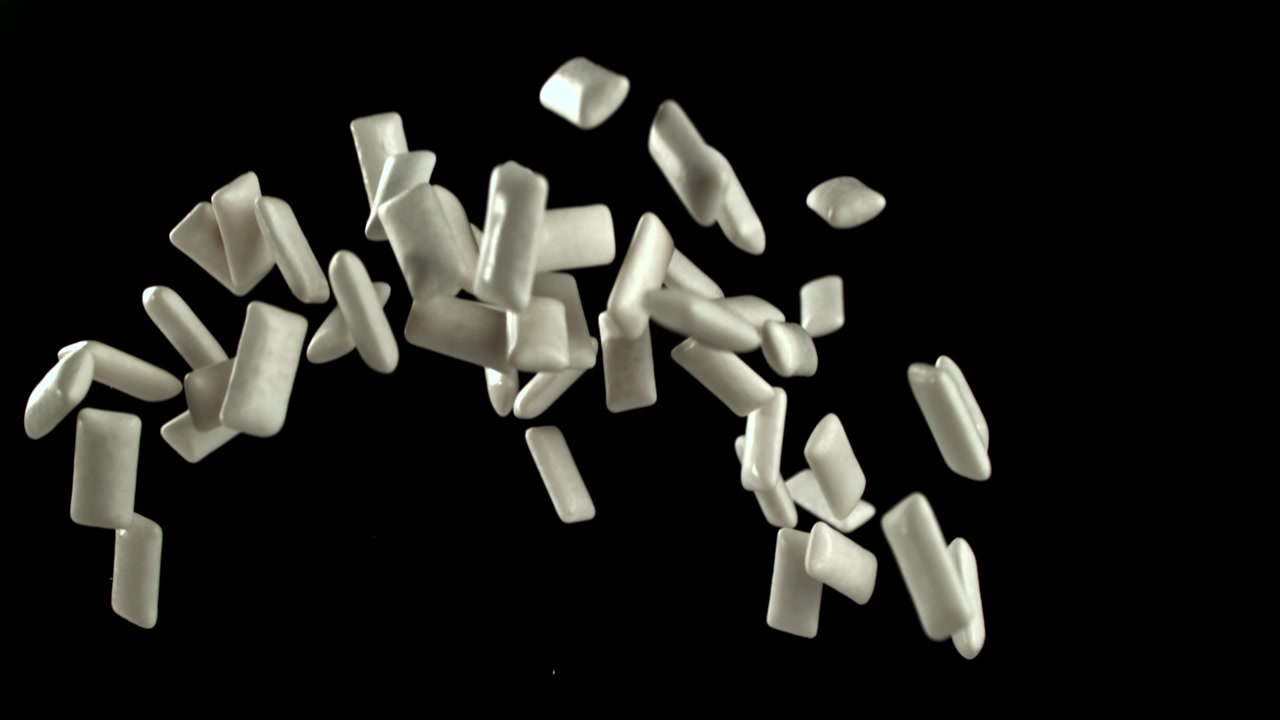 White Chewing Gum Pieces Floating Upwards in Slow Motion on Black Background