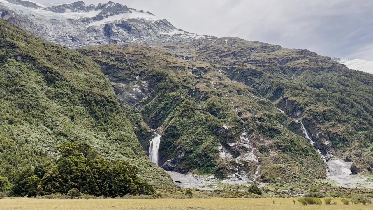Vista panoramica di imponenti cime alpine con neve, ghiacciai e cascate, circondate da aspre montagne verdi. Splendide riprese della natura dell'Isola del Sud