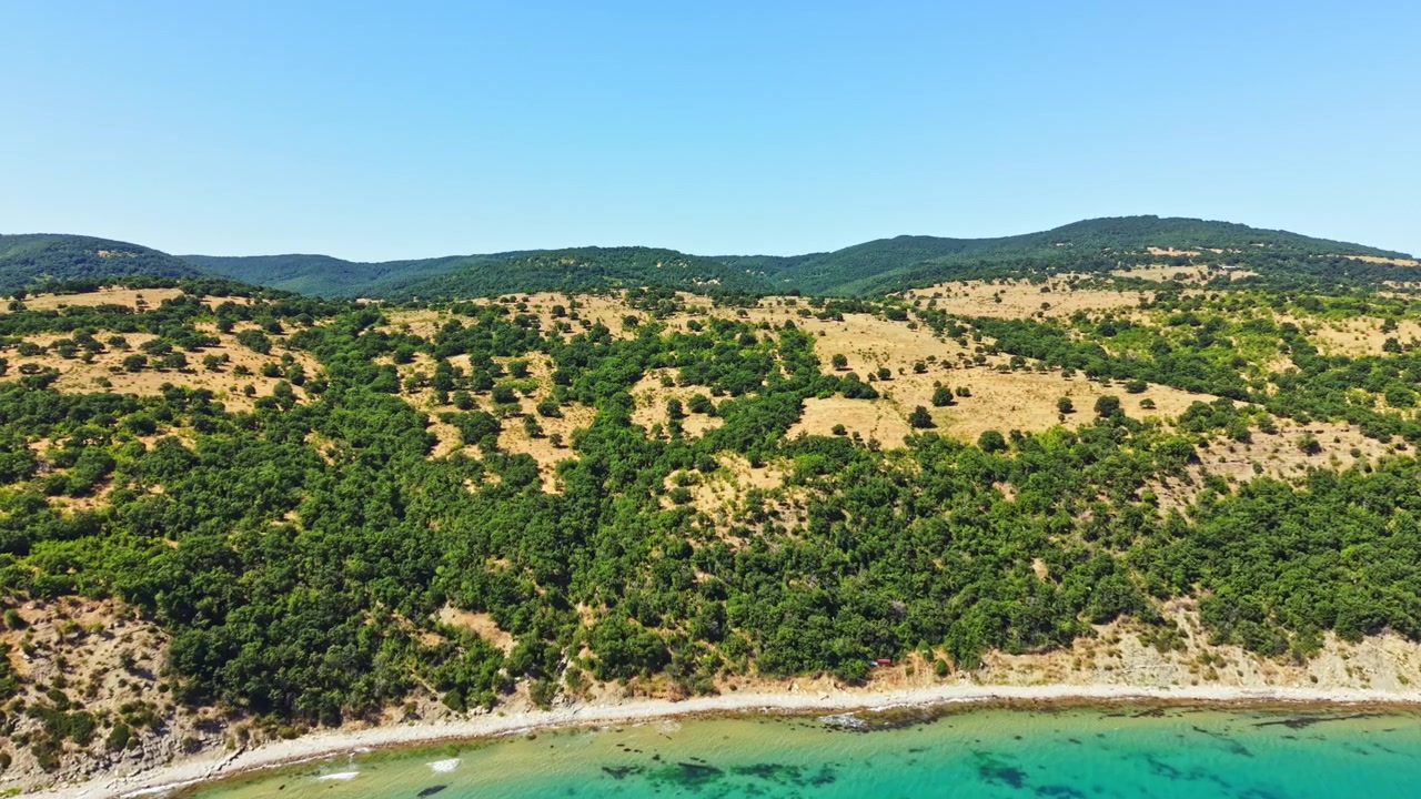 Ampia vista di una costa rocciosa e colline verdi sotto un cielo sereno vicino alla spiaggia a mezzogiorno in estate