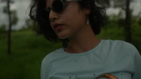 Close-up-shot-of-an-Indian-young-girl-surrounded-by-the-forest-of-India,-she-takes-a-moment-to-comb-her-hair-while-wearing-stylish-sunglasses