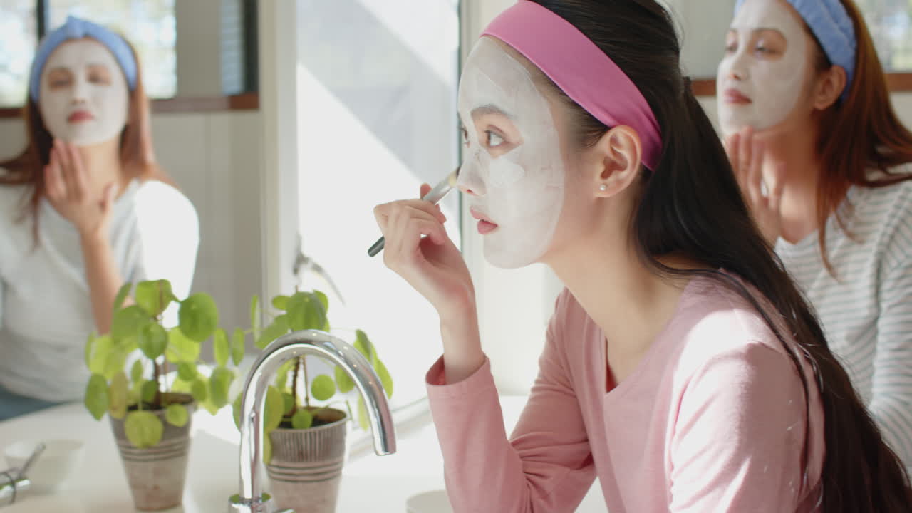 Applying face mask, asian mother and daughter enjoying skincare routine together in bathroom