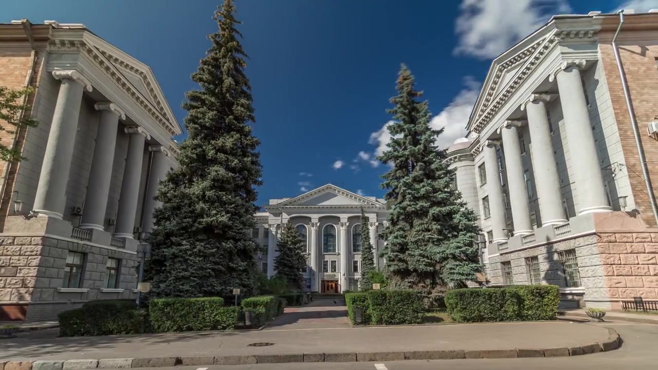 Harkovan kansallisen radioelektroniikan yliopiston etunäkymä – vanha rakennus pääsisäänkäynteineen, kuvattuna timelapse-hyperlapsena, Harkova, Ukraina. Sininen pilvinen taivas mäntypuineen.