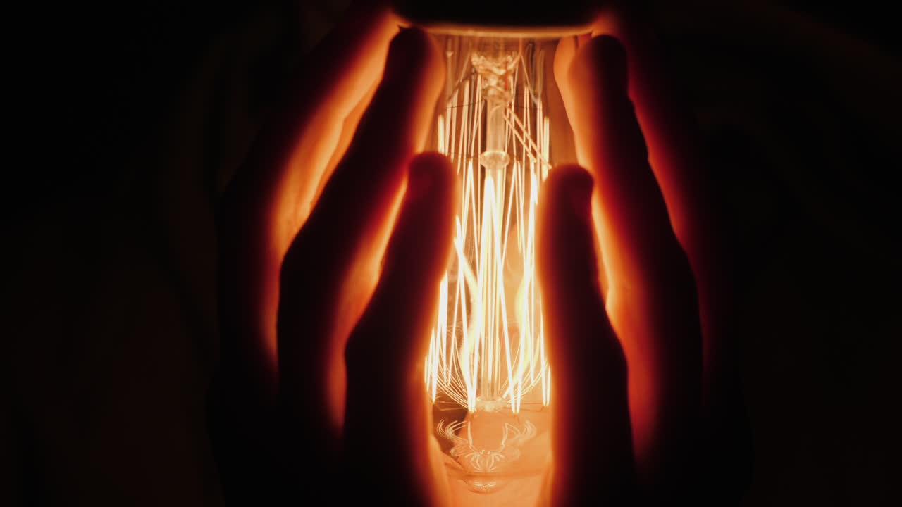 사람의 뒷모습은 어둠 속에서 전구 근처에서 손을 따뜻하게 한다