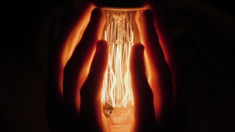 back view of man warms his hands near a light bulb in the dark