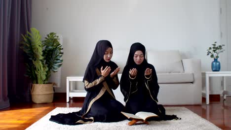 young muslim woman and female friend reading quran and praying