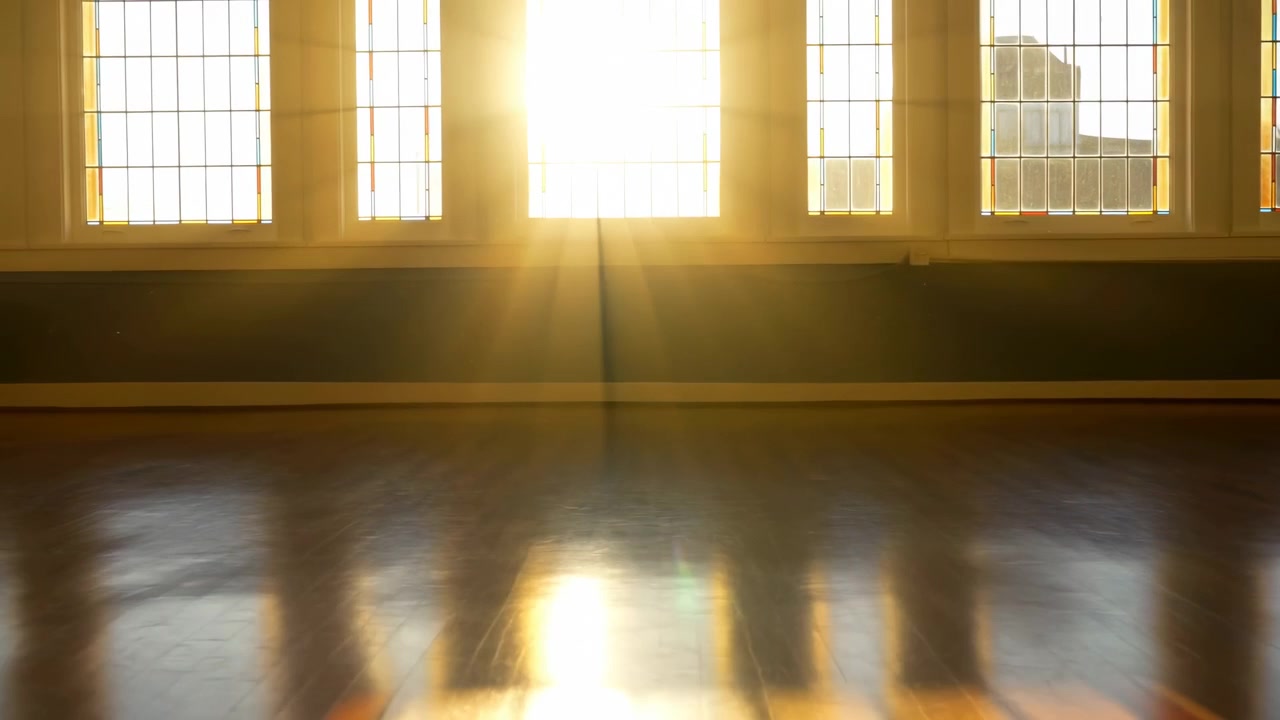 Slow lateral movement reveals an unfurnished room with large multipane windows, colored edge accents, sun rays, deep wall shadows, and glowing reflections stretching across dark wood flooring.