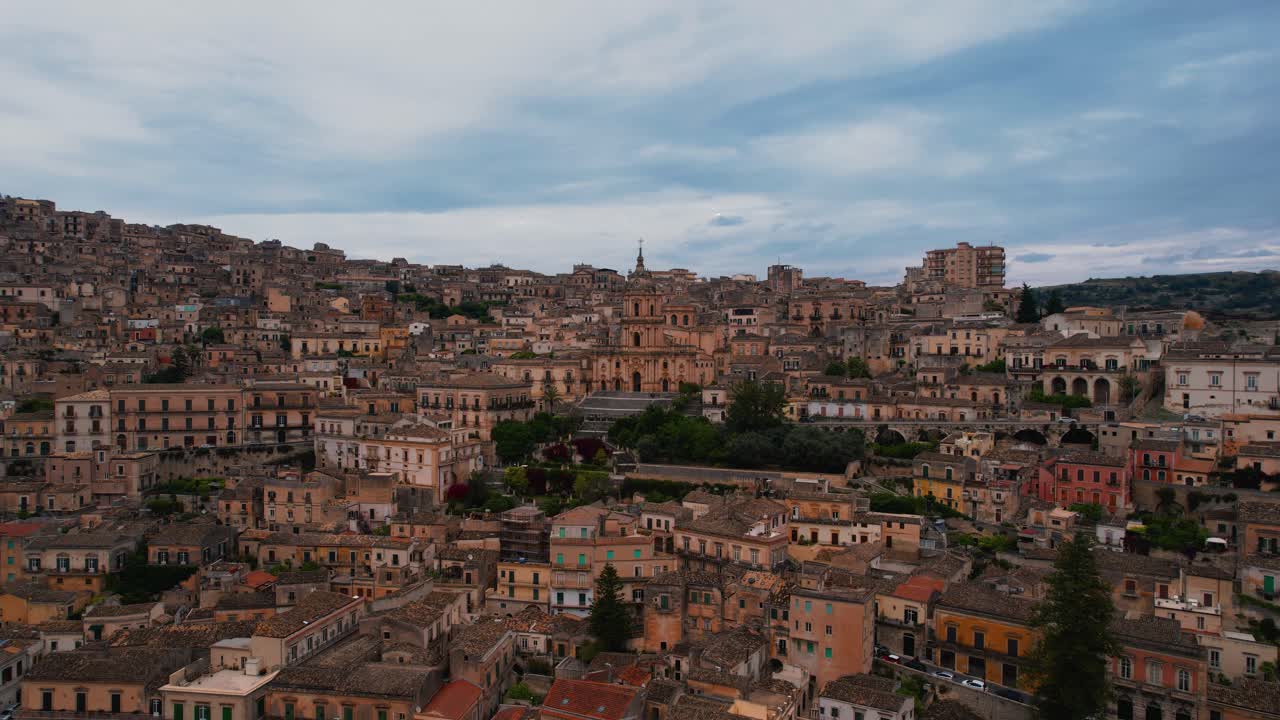 Circling Duomo di San Giorgio with Modica old town buildings. Historic architecture, Sicily aerial.