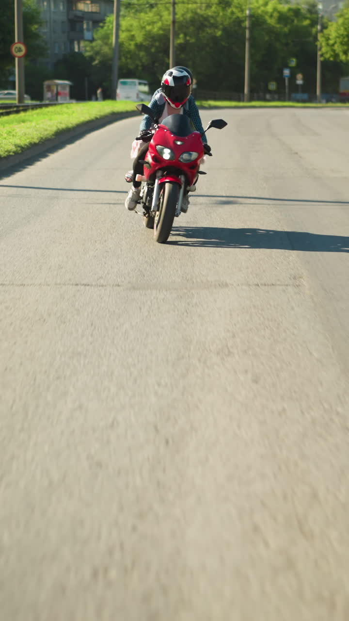 dos parientes viajan en una bicicleta eléctrica con cascos, navegando por una carretera, se ve un coche de color ceniza delante de ellos mientras viajan, con árboles y postes eléctricos en el fondo