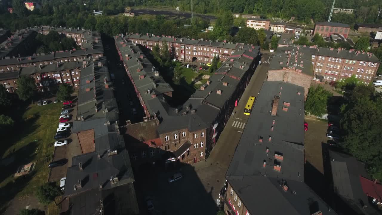 Dynamic drone shot of a historic Silesian settlement, featuring streets, a moving bus, a forest, and rooftops with chimneys, in 4K