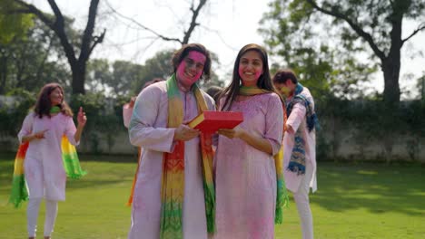 indian couple posing with a sweet box on holi