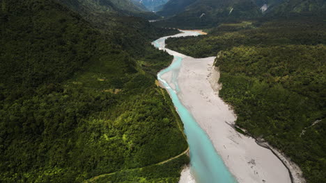 aerial revealing shot of the majestic mountains surrounding a beautiful green valley with a blue winding river in the middle, new zealand