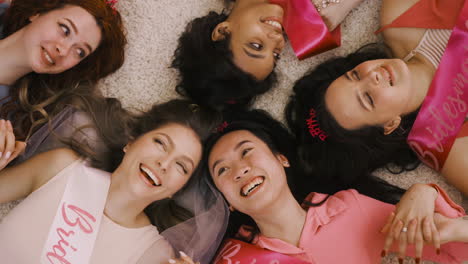 top view of bachelor girl and her friends holding hand lying on the carpet 2