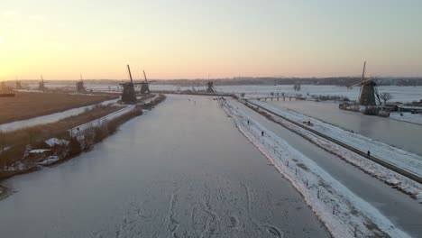 Stunning-golden-sunshine-at-Kinderdijk-windmills-with-people-ice-skating,-winter