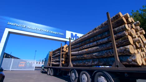 un camión de madera con un remolque está completamente cargado de troncos se conduce a través de la entrada al territorio de la planta de carpintería