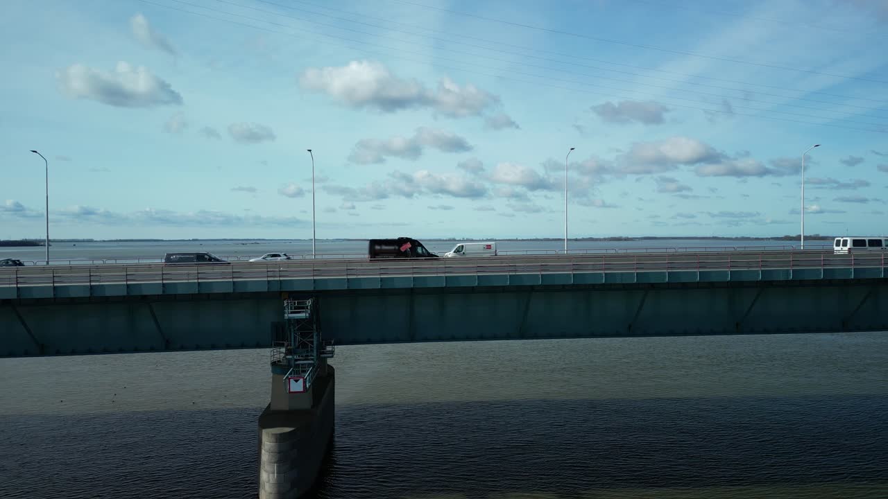 드론은 교통량이 많은 다리 옆 강 위를 옆으로 날아갑니다.