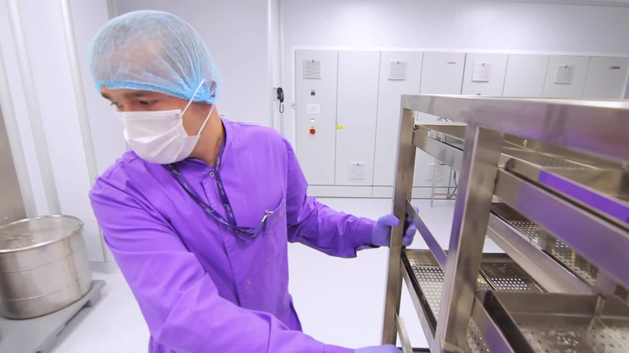 보호 마스크와 살균복을 입은 남자가 금속 창고 선반을 움직입니다.