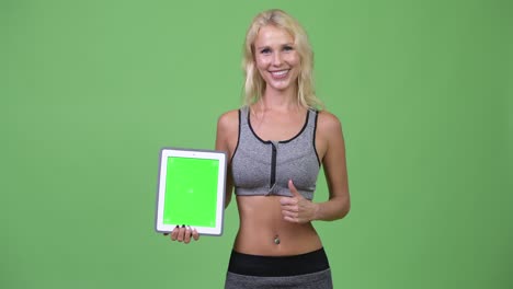 young happy beautiful woman showing digital tablet and giving thumbs up ready for gym