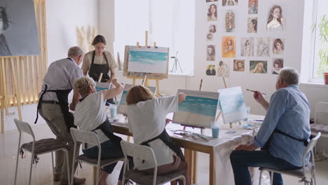 vista de ángulo alto de amigos mayores alegres pintando en lienzo. mujer mayor sonriendo mientras dibuja con el grupo. mayores asistiendo a clase de pintura juntos. hombres mayores divirtiéndose pintando en clase de arte