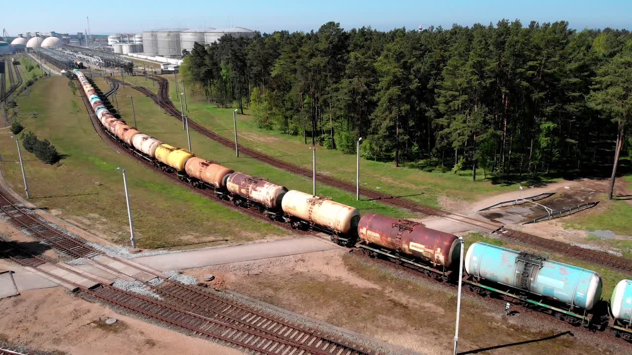 Drone footage of a freight train carrying tanks moving slowly along railway tracks on a sunny day. Industrial transport scene captured from above with clear weather and smooth motion