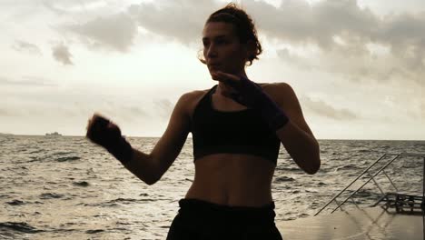 female boxer makes sidekick of her legs against the son by the sea in slow motion. beautiful female boxer training on the beach