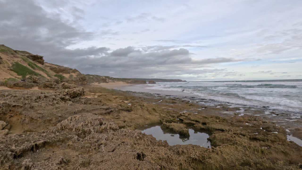 olas chocando contra la orilla rocosa con piscinas de marea