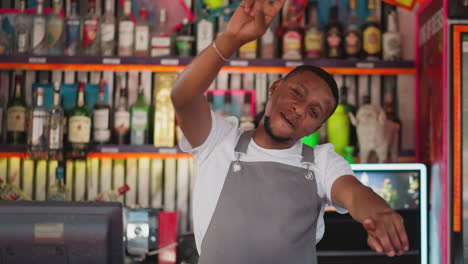 el barman feliz baila en la encimera del club. el barman afroamericano alegre muestra un gesto de paz en el club nocturno en una fiesta. el camarero negro se divierte en el trabajo
